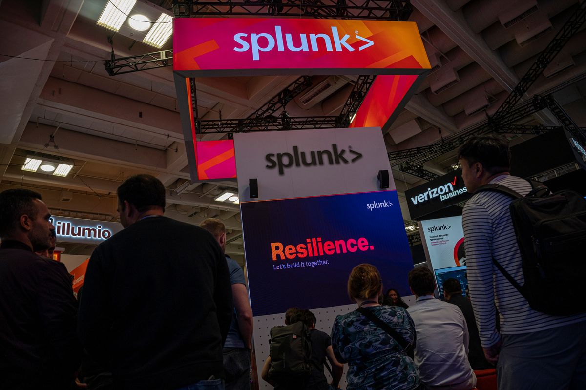 The Splunk logo on a stand at a conference, on a lit up neon sign.