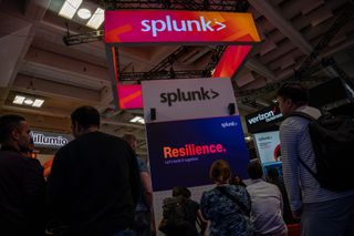 The Splunk logo on a stand at a conference, on a lit up neon sign.