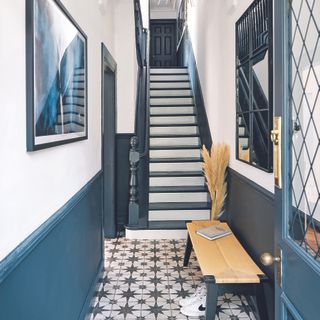 Hallway with navy walls, bench, mirror and tile flooring.