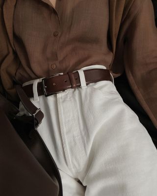 Woman wearing white jeans with a brown classic belt and a tucked-in brown button-down.