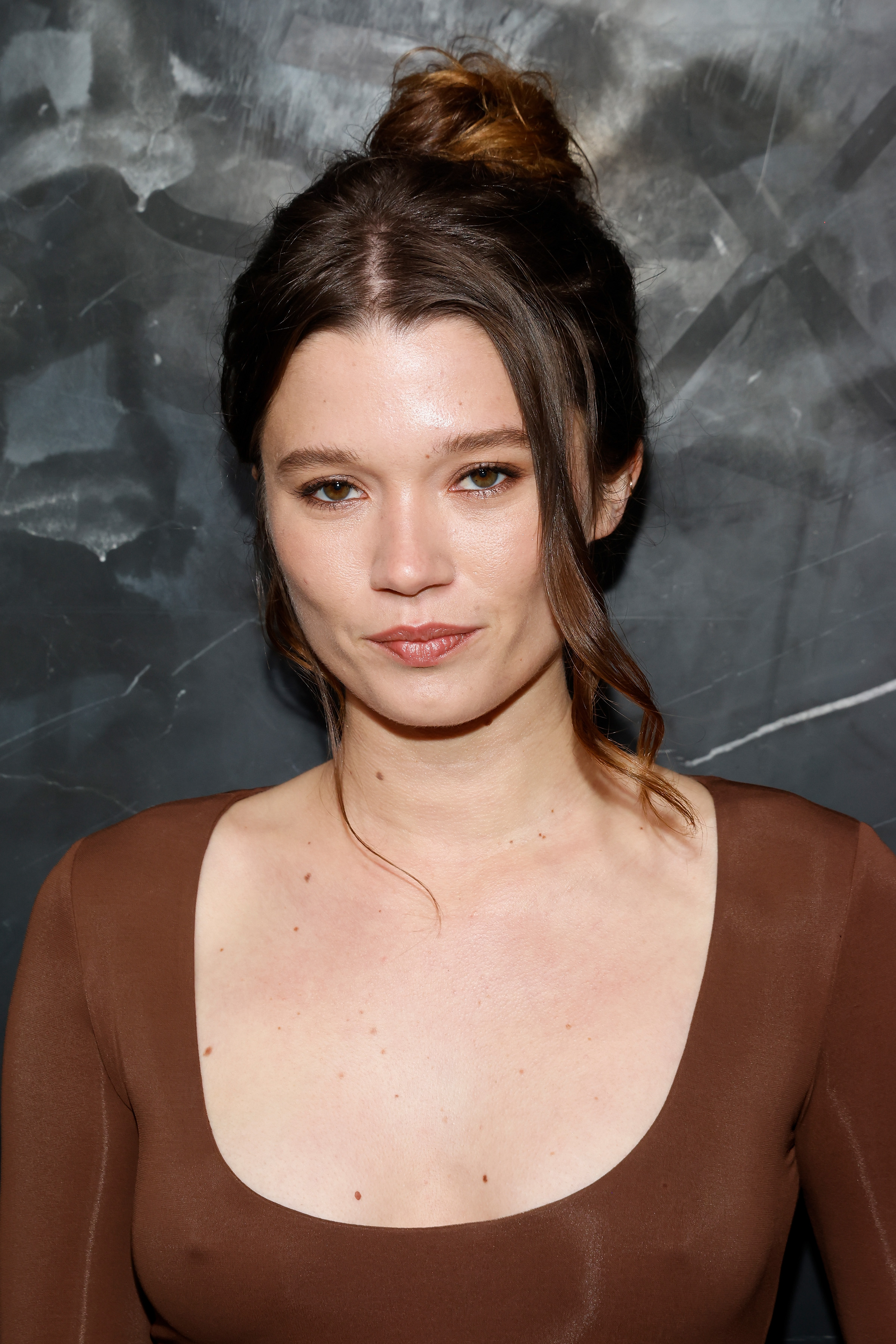 rain spencer poses on a red carpet at the michael kors 2024 new york fashion week show wearing a brown long sleeved top and with her hair up in a bun