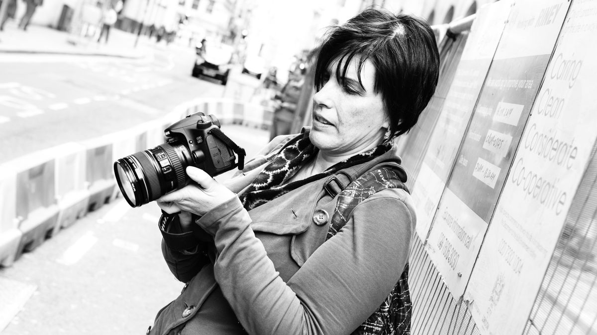 A woman standing on a street holding a Canon EOS 60D