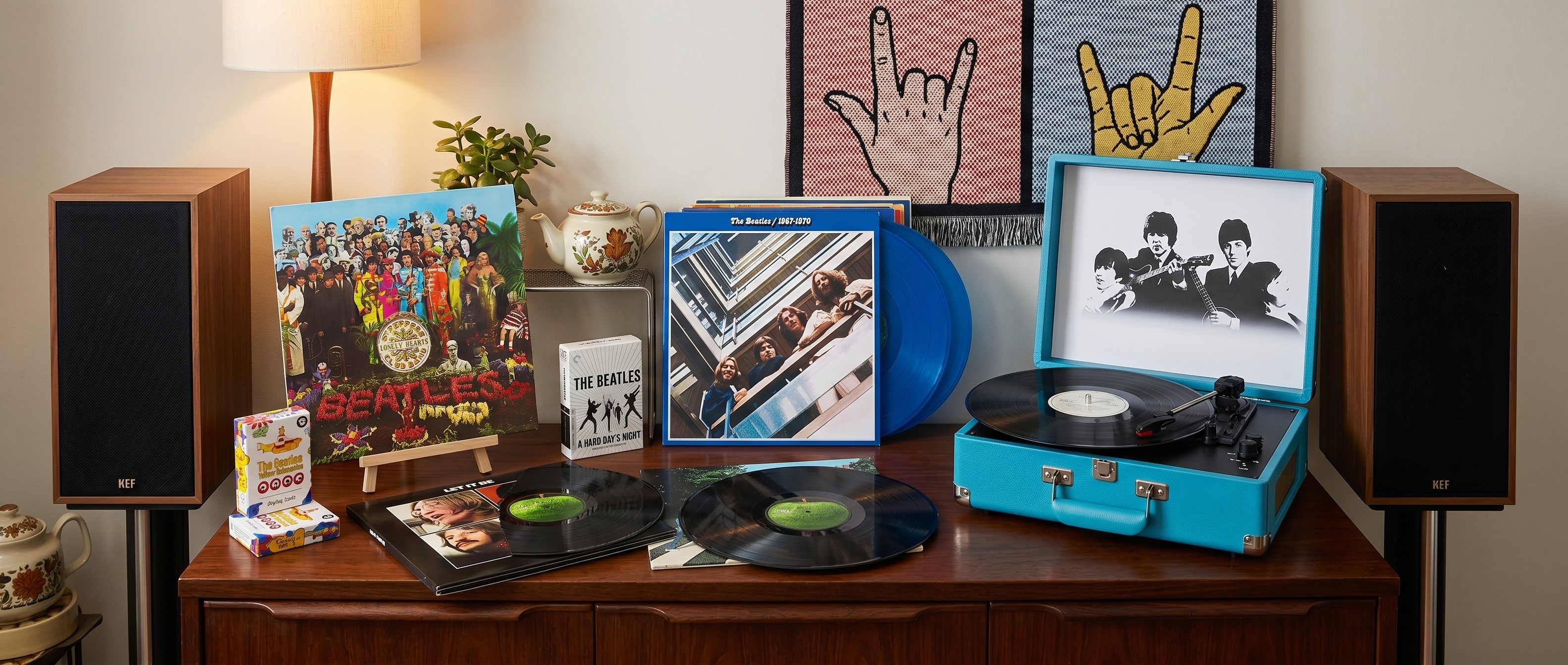 Seveal Beatles vinyl albums on a wooden sideboard, with a Beatles-branded suitcase turntable, plus some Beatles playing cards and A Hard Day's Night on Blu-ray
