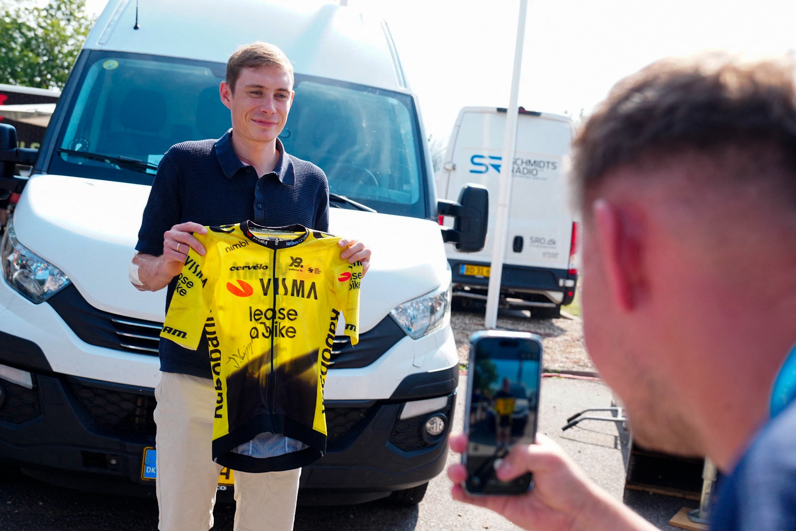 Jonas Vingegaard holds up a signed Visma-Lease a Bike jersey while being videoed
