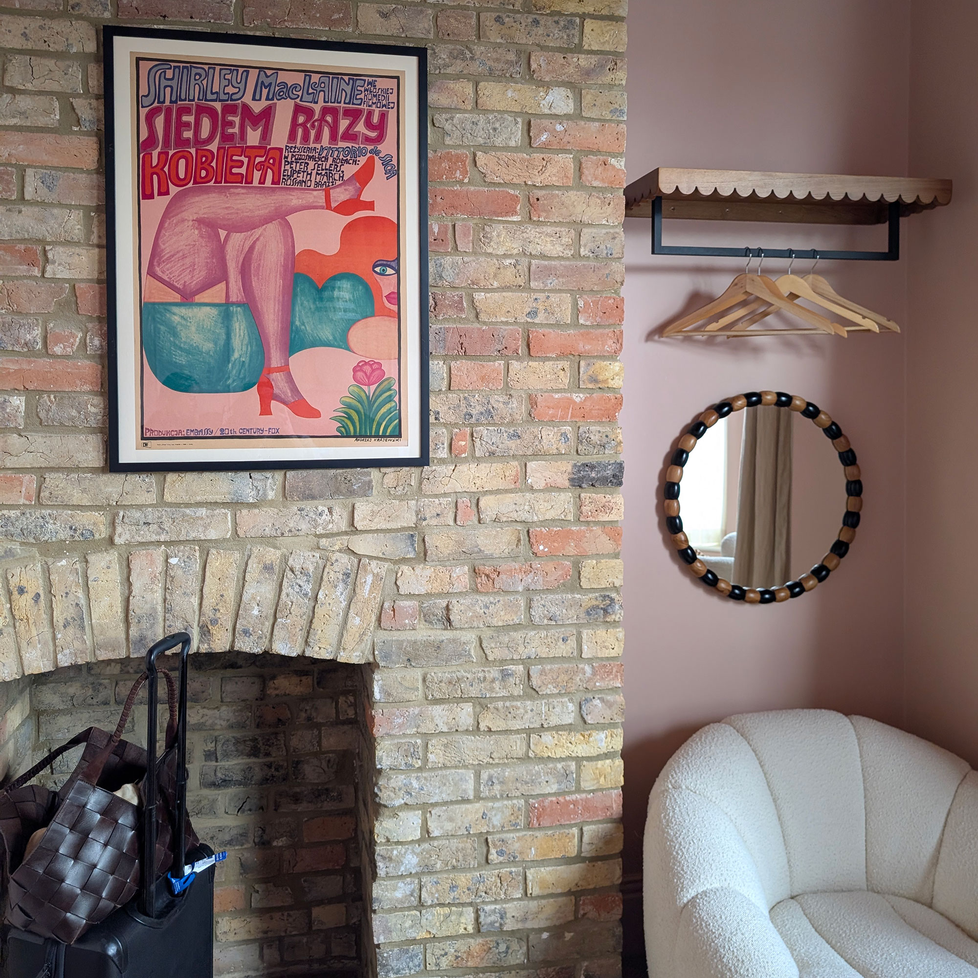 Framed pink graphic poster hung on brick fireplace wall beside open clothes rail