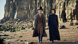 Max Irons in a long coat and top hat as Henry Hobday walks on the beach with Synnøve Karlsen in black dress and bonnet as Cassy in Miss Austen.