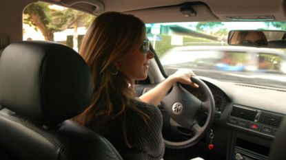 A woman at the wheel of her car, wearing sunglasses.