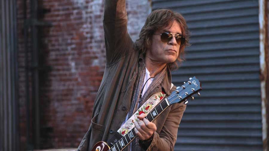 Rick Ventura in an alley playing guitar with one arm held high