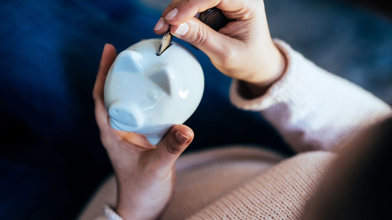 A woman&#039;s hands hold a piggy bank while putting a coin into it.