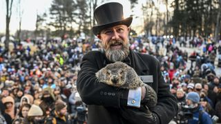 A man in a suit and top hat holds a groundhog in front of a large crowd.