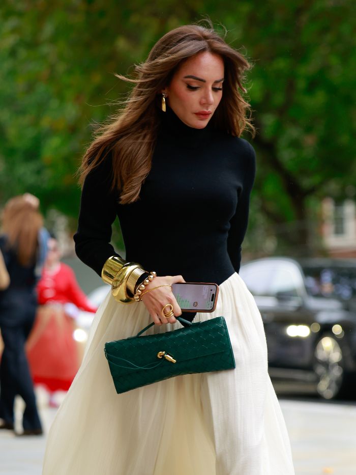 A woman at London Fashion Week wearing a cream skirt and a black top with brunette hair and golden highlights