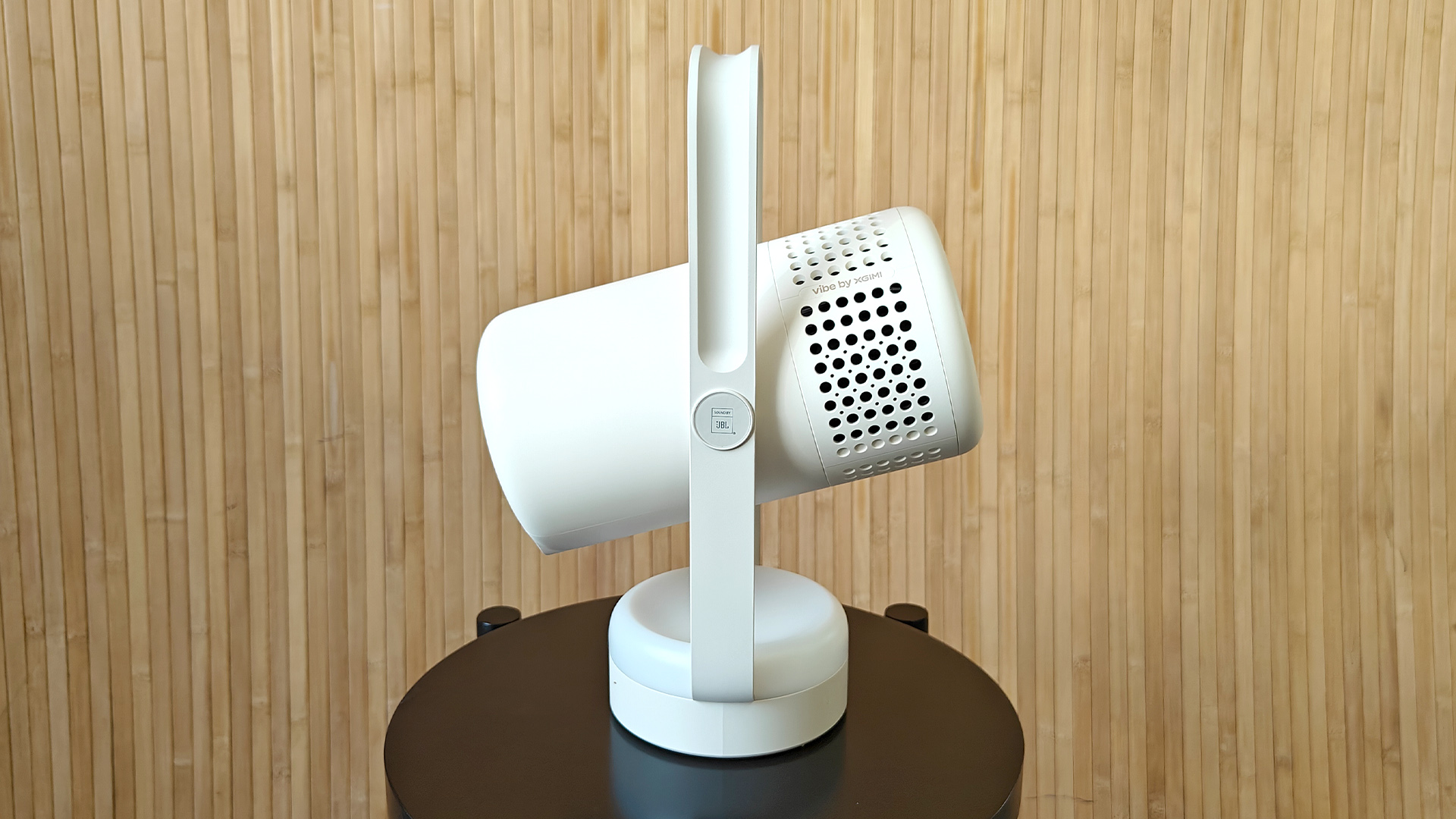 Xgimi Vibe One portable projector on small black table in front of bamboo wall viewed from side
