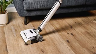 the gtech airram 3 vacuum cleaner with white wide base and an adjustable handle shown cleaning on rugs and wooden floors