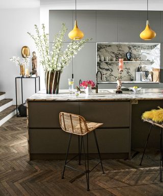 Modern grey kitchen with yellow accents in the pendant lighting and cushions, rattan bar stools and a large vase of white flowers.