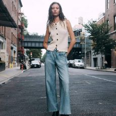 A model wearing a cream knitted vest and jeans from rag & bone in front of a city backdrop.