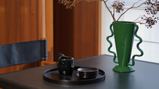 Wavy daul-handled green vase sitting on a sleek black table in a warm, room-paneled dining room