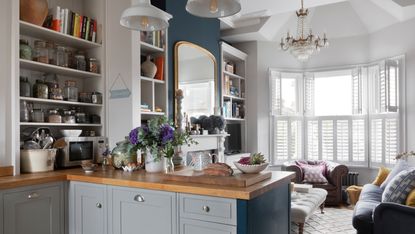 Pippa Jones house: shot from kitchen into living room with big bay window, white shutters, and dark blue feature wall with oversized mirror over white fireplace