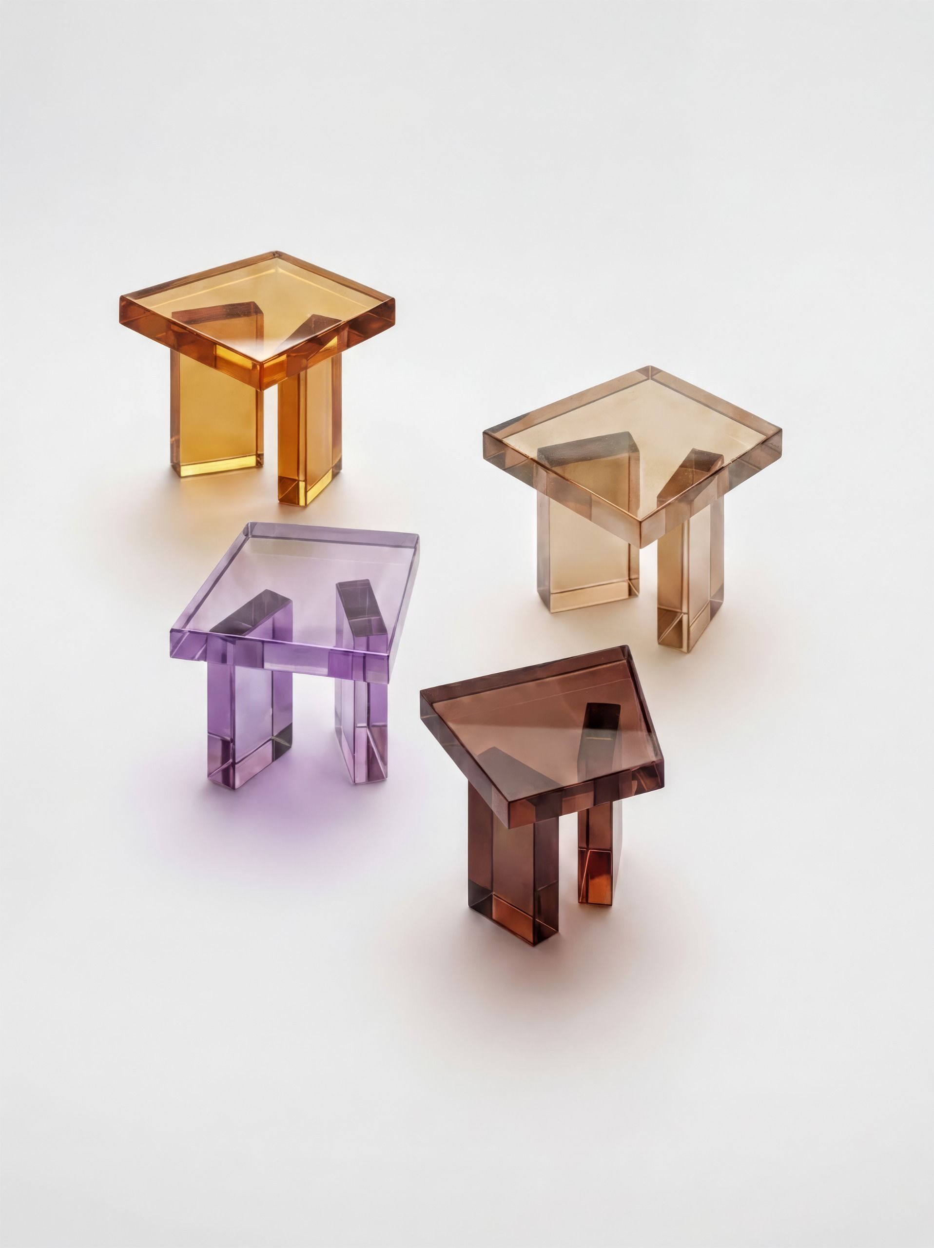 Four resin chairs in semi-transparent finishes, in amber, purple, brown, and beige, styled against a white floor and seen from above.