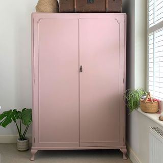 Pink painted wardrobe against white wall next to window with pot plants