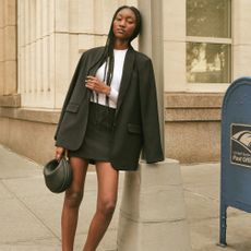A black woman wearing a black skirt and blazer standing on a street