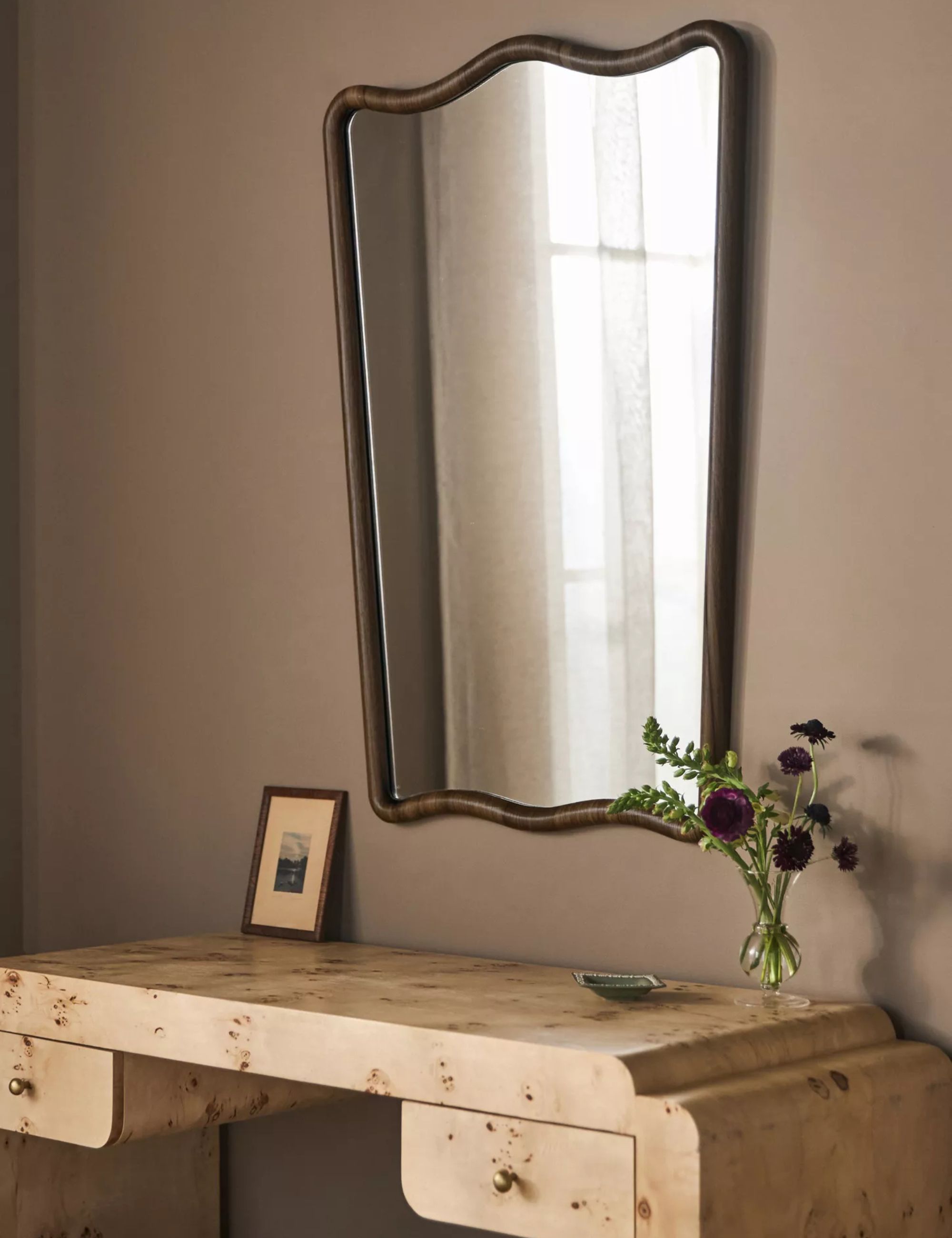 Wooden mirror above a burl wood dressing table against pale brown wall