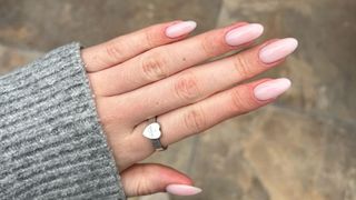 A close-up of Sennen Prickett's hand which features milky pink almond nails, taken above a pavement background