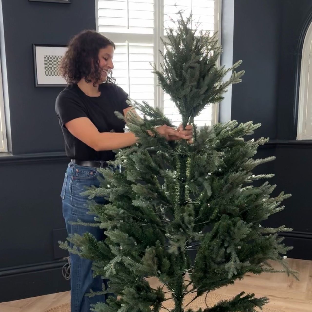 Sara Hesikova putting up an artificial Christmas tree in a black-painted living room