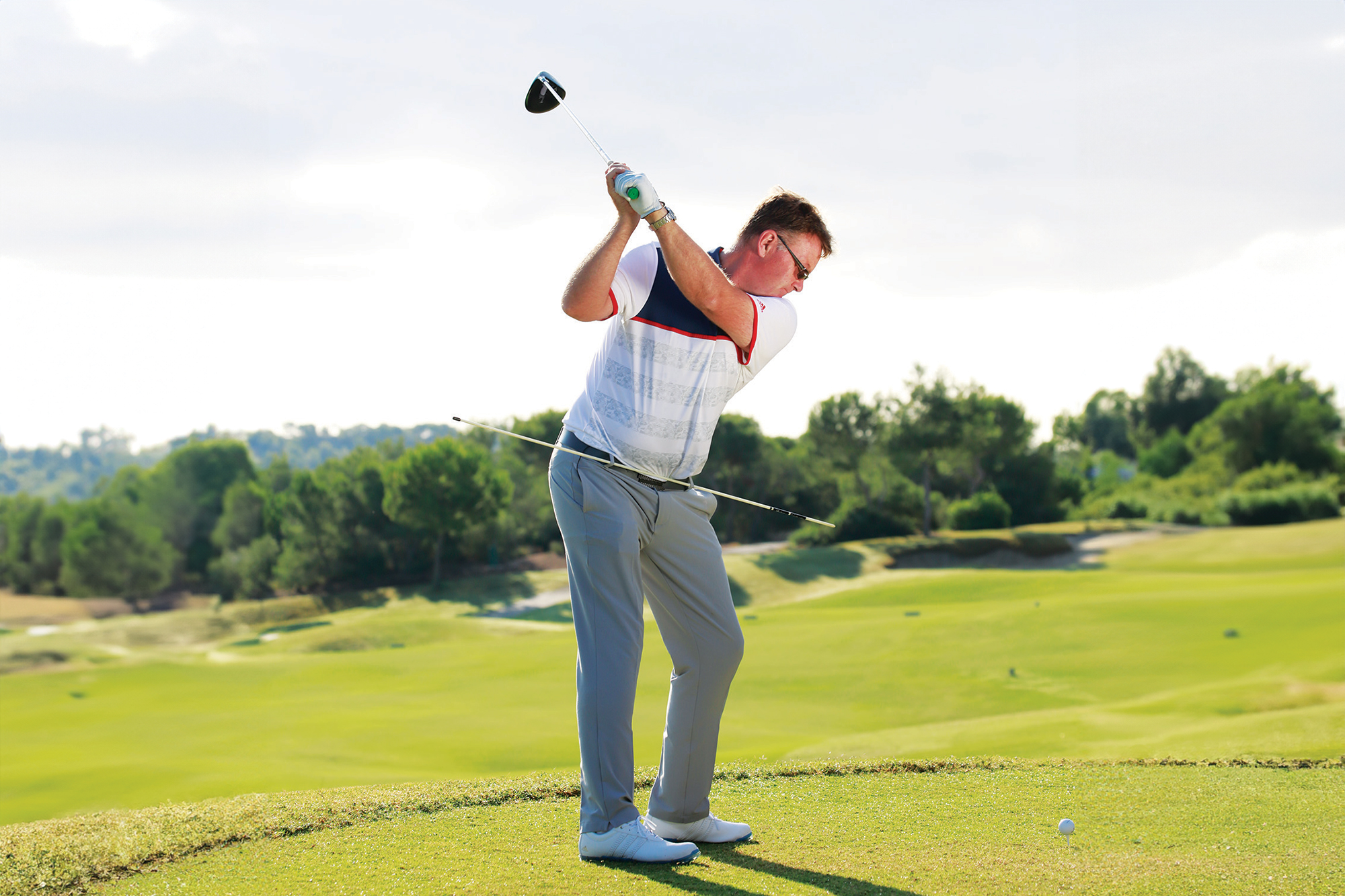 A demonstration of hip rotation in the golf swing, with an alignment stick through the belt loops as a drill to visually identify the correct angle for the hips at the top of the backswing