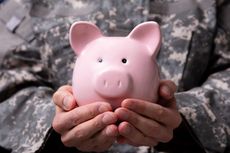 A person in a military uniform holds a piggy bank. 