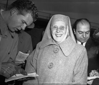 Princess Alice of Greece smiles broadly and wears a large overcoat and a nun's habit