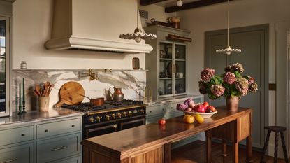 A traditional kitchen with mid-blue cabinets, white walls, a marble countersplash, a wooden island, and vintage vessels on the counters