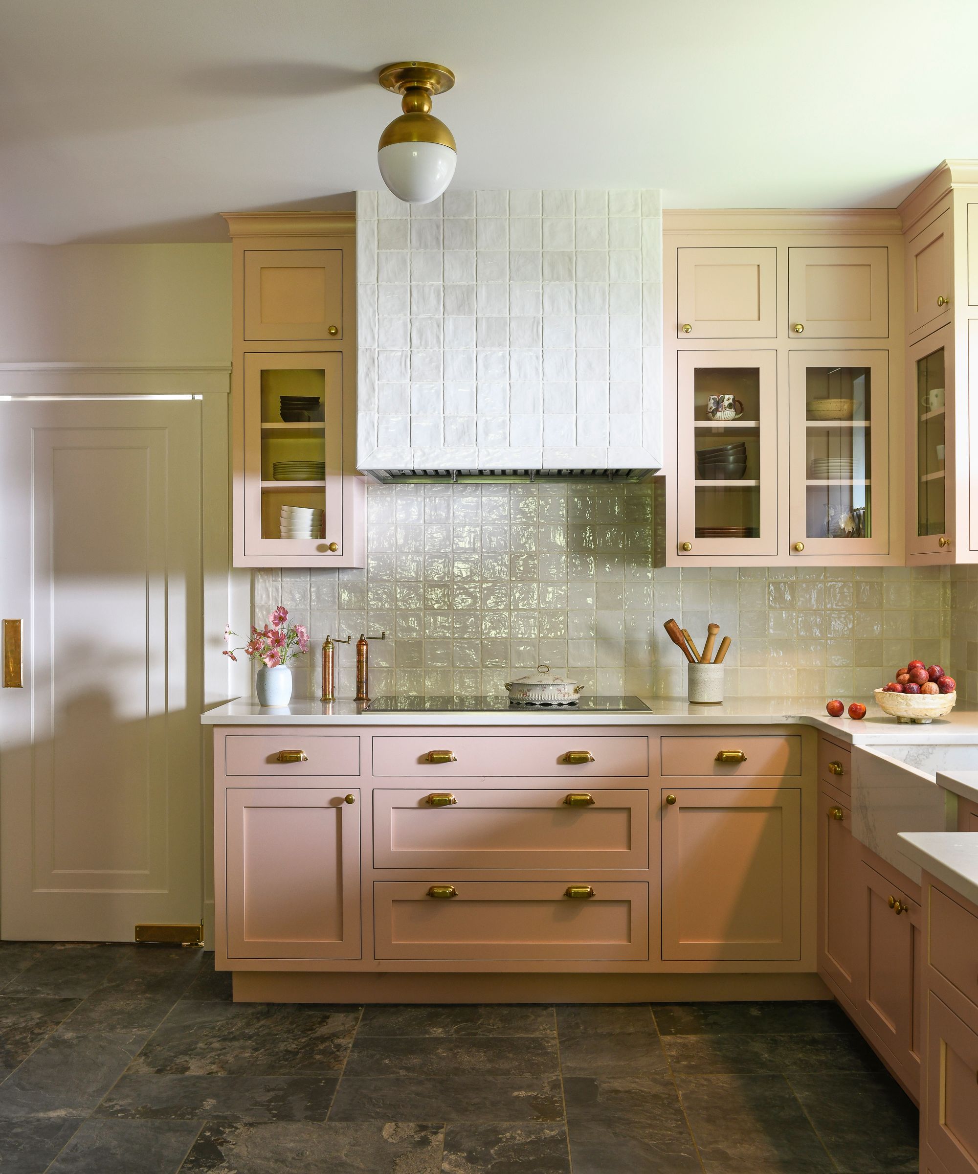 A kitchen with pale pink cabinets, warm white tiles, and gray tiled flooring.