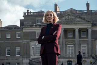 allison janney as grace penn standing in front of a british government building and wearing a red suit in the diplomat season 2