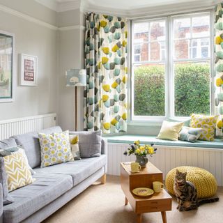 living room with white wall and grey colour sofa and yellow floral printed curtain