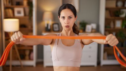 Woman holds resistance band in front of her in domestic setting