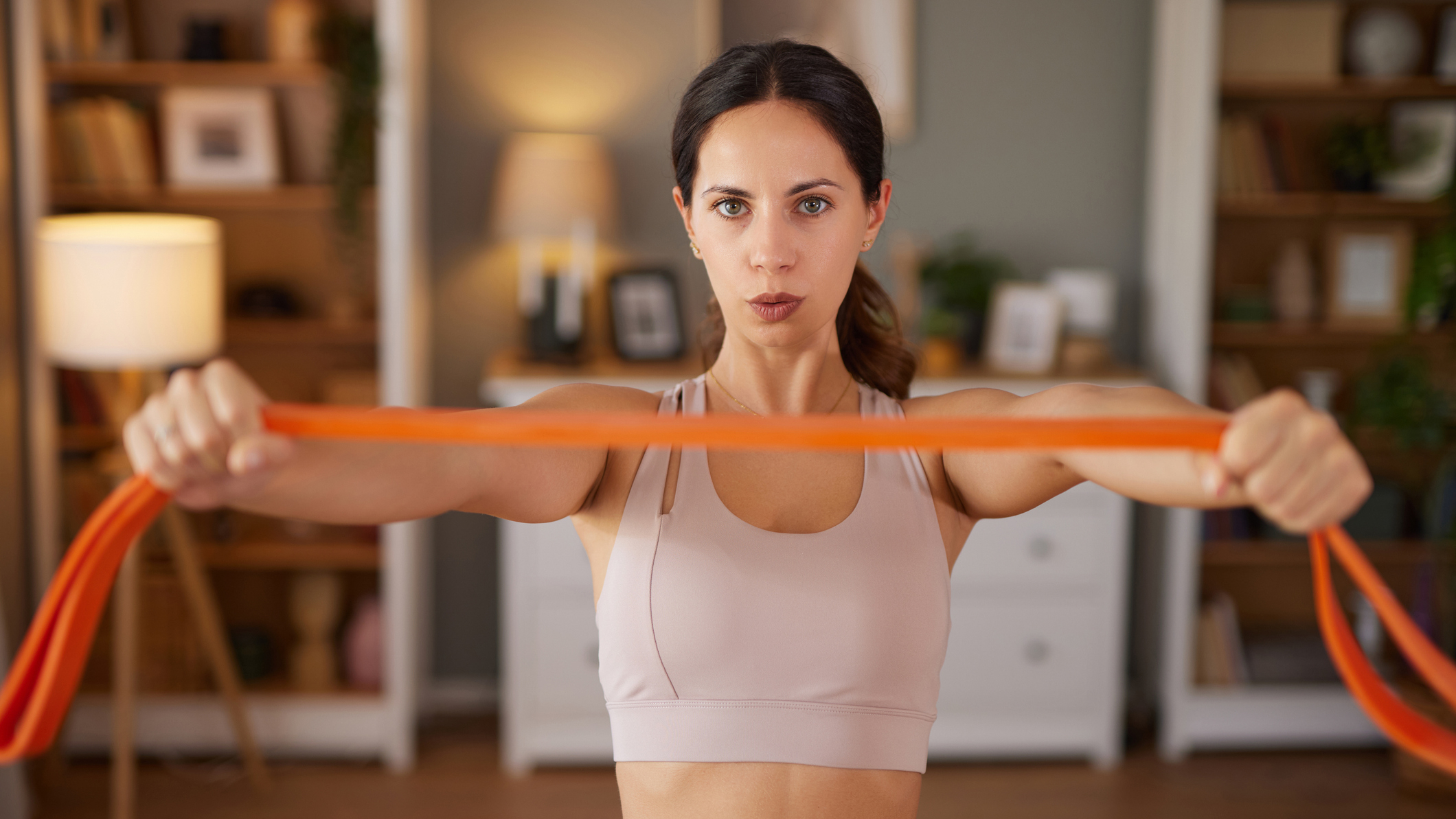 Woman holds resistance band in front of her in domestic setting