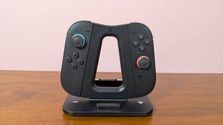 Genki Dual Wield Nintendo Switch 2 Charging Station with Joy-Cons attached, on a desk with pink wall in background