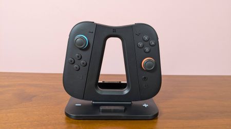 Genki Dual Wield Nintendo Switch 2 Charging Station with Joy-Cons attached, on a desk with pink wall in background