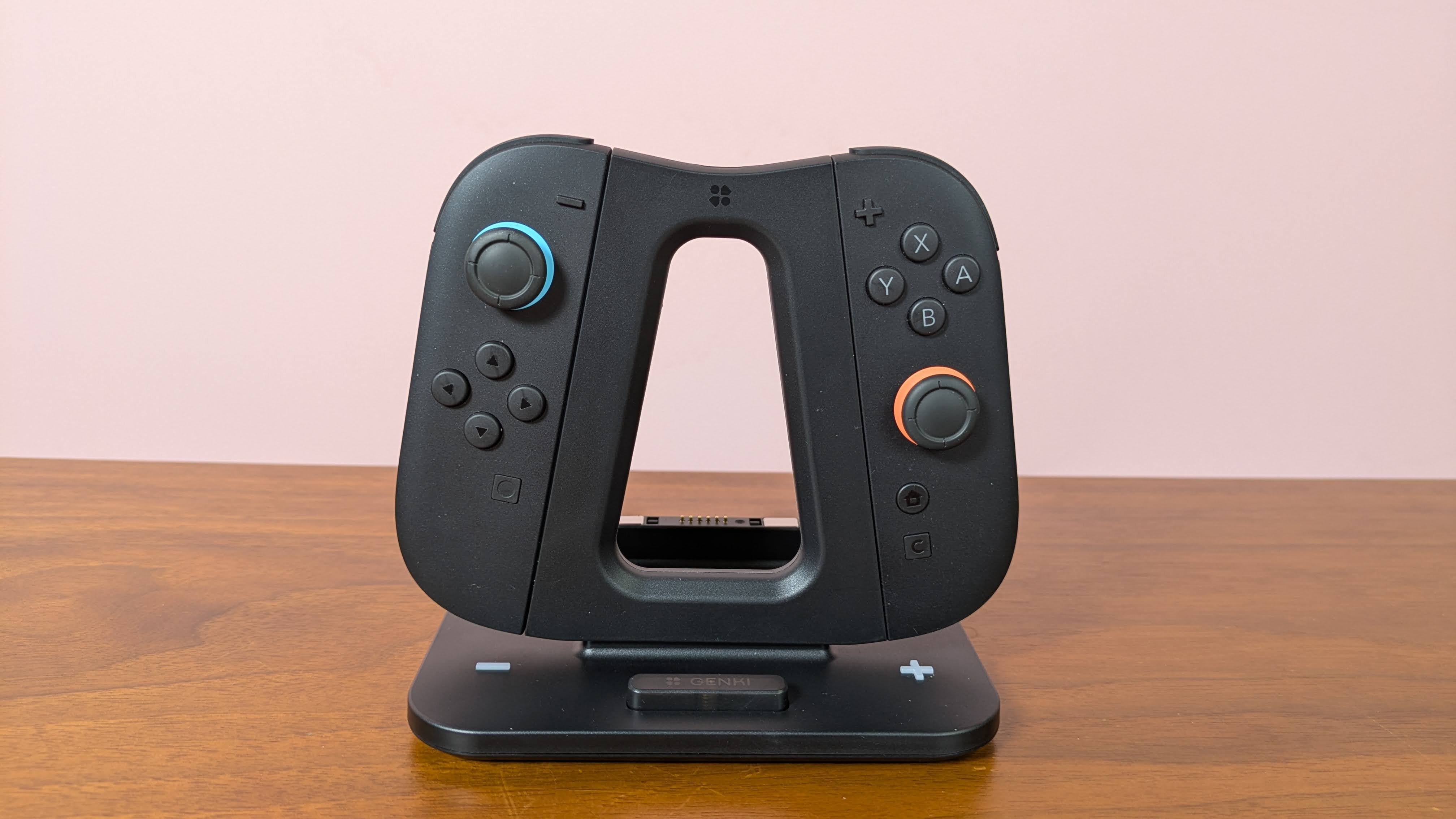 Genki Dual Wield Nintendo Switch 2 Charging Station with Joy-Cons attached, on a desk with pink wall in background
