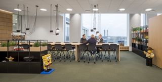 Three people sat a long meeting table inside a Lego buillding