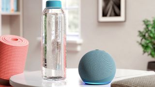 The Amazon Echo Dot (2020) in blue pictured on a white surface next to a water bottle