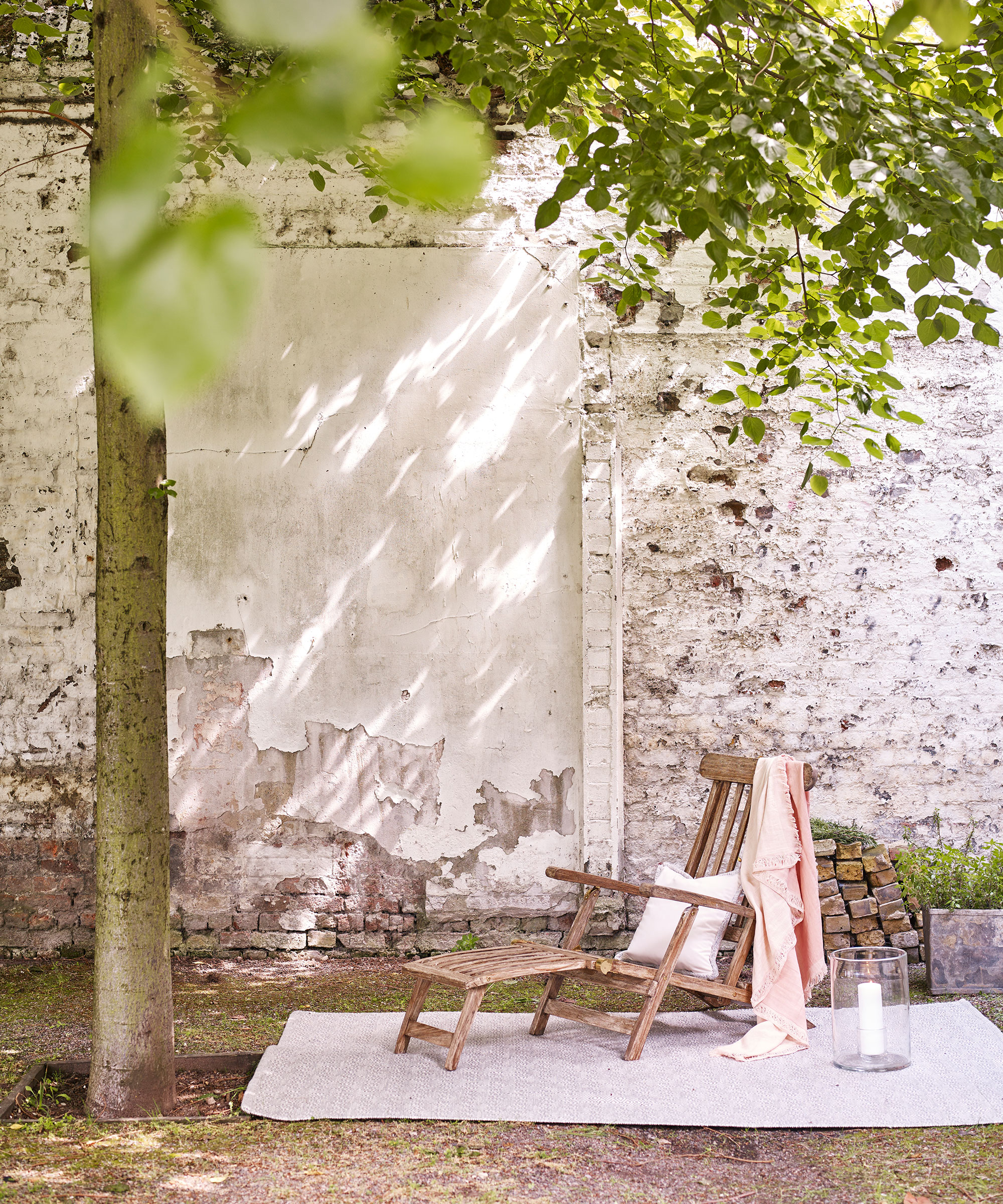 A shaded area of a garden with a wooden sun lounger below trees