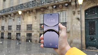 The Oppo Find X8 Pro against some buildings, with the display on and lockscreen visible