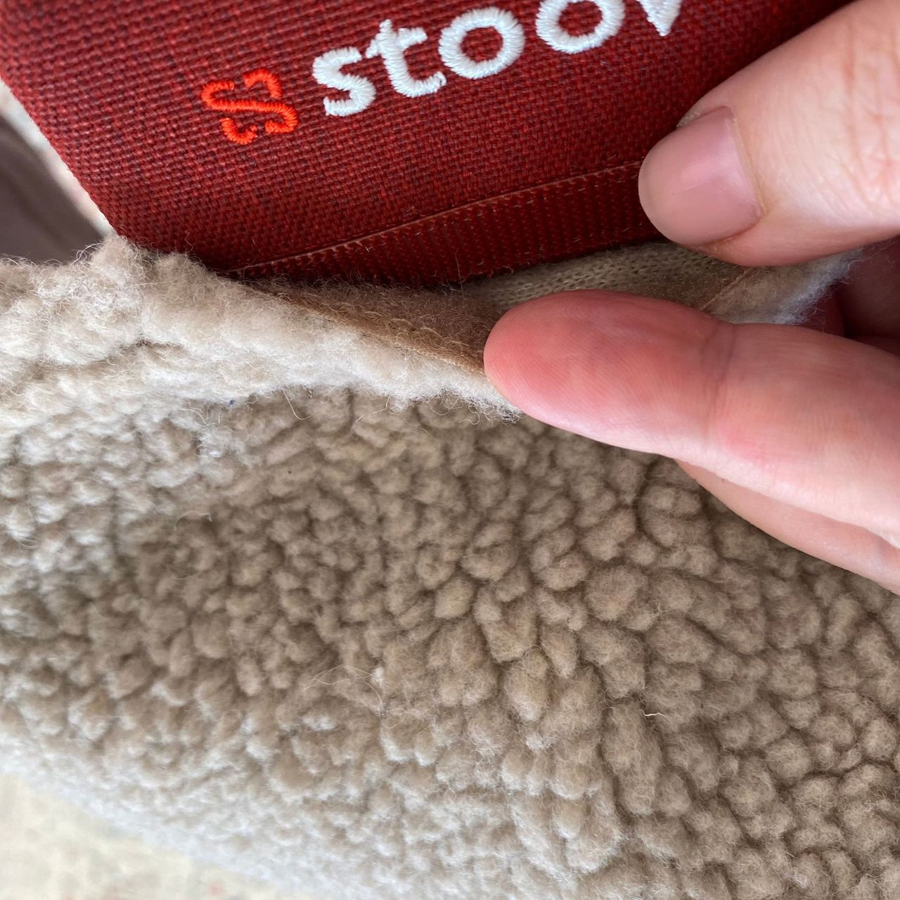 Hand undoing the velcro attaching the Stoov Big Hug3 woolly cover to the smart label