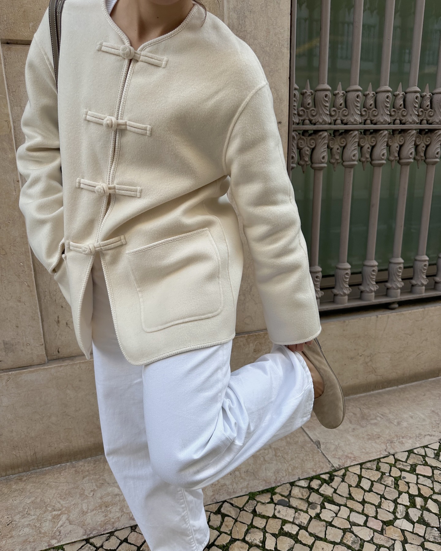 Influencer Debora Brosa wears a wool front-closuer jacket, white pants, and pale suede ballet flats.