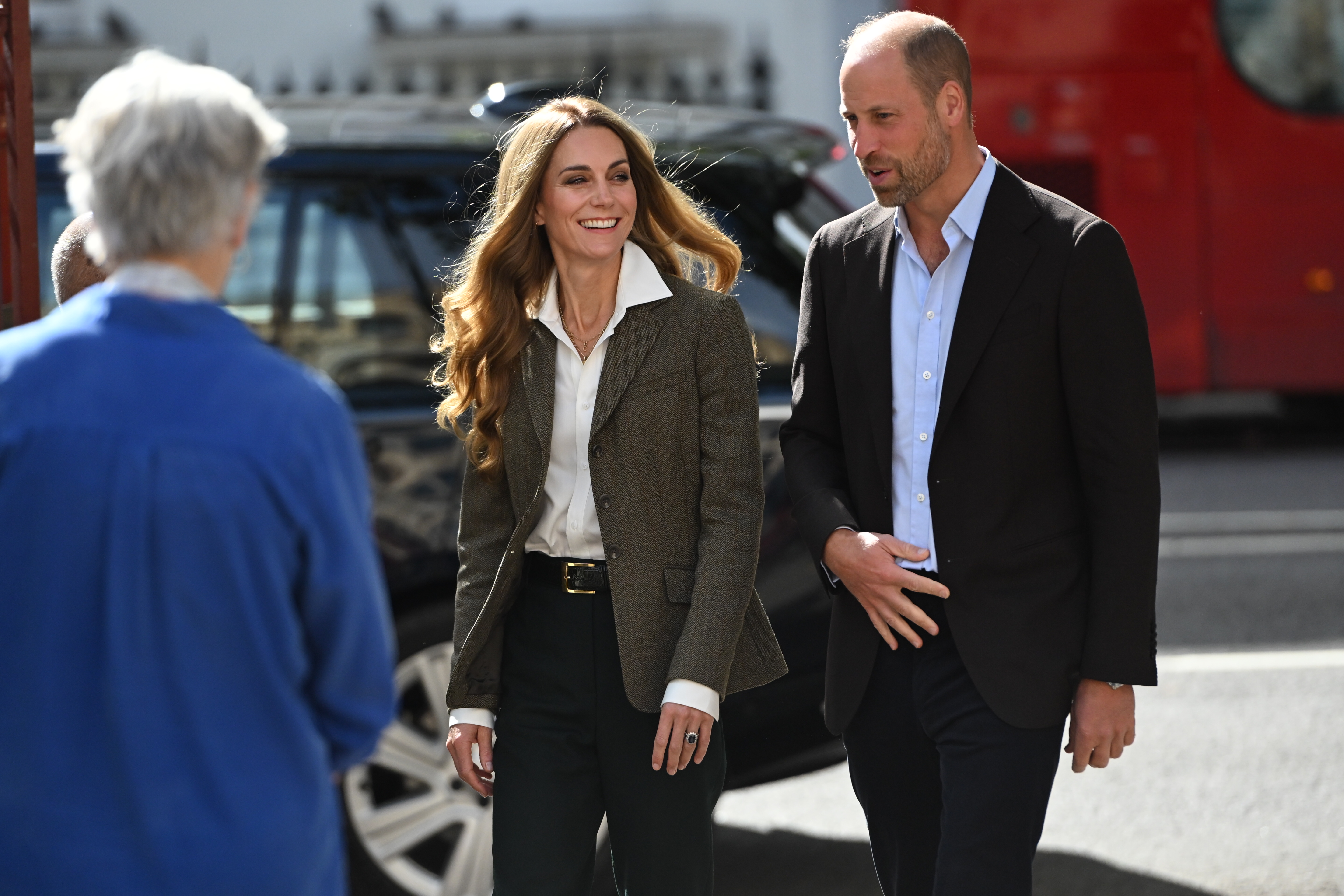 Kate Middleton and Prince William wearing blazers and smiling walking outside by a car