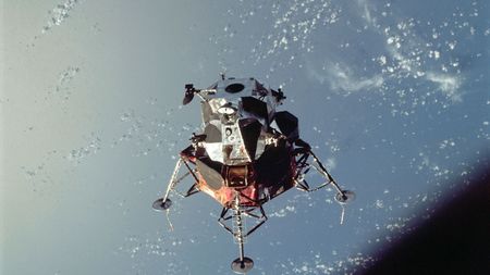 a moon lander with four legs hovers above Earth.