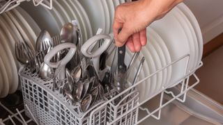 Someone loading cutlery into a dishwasher