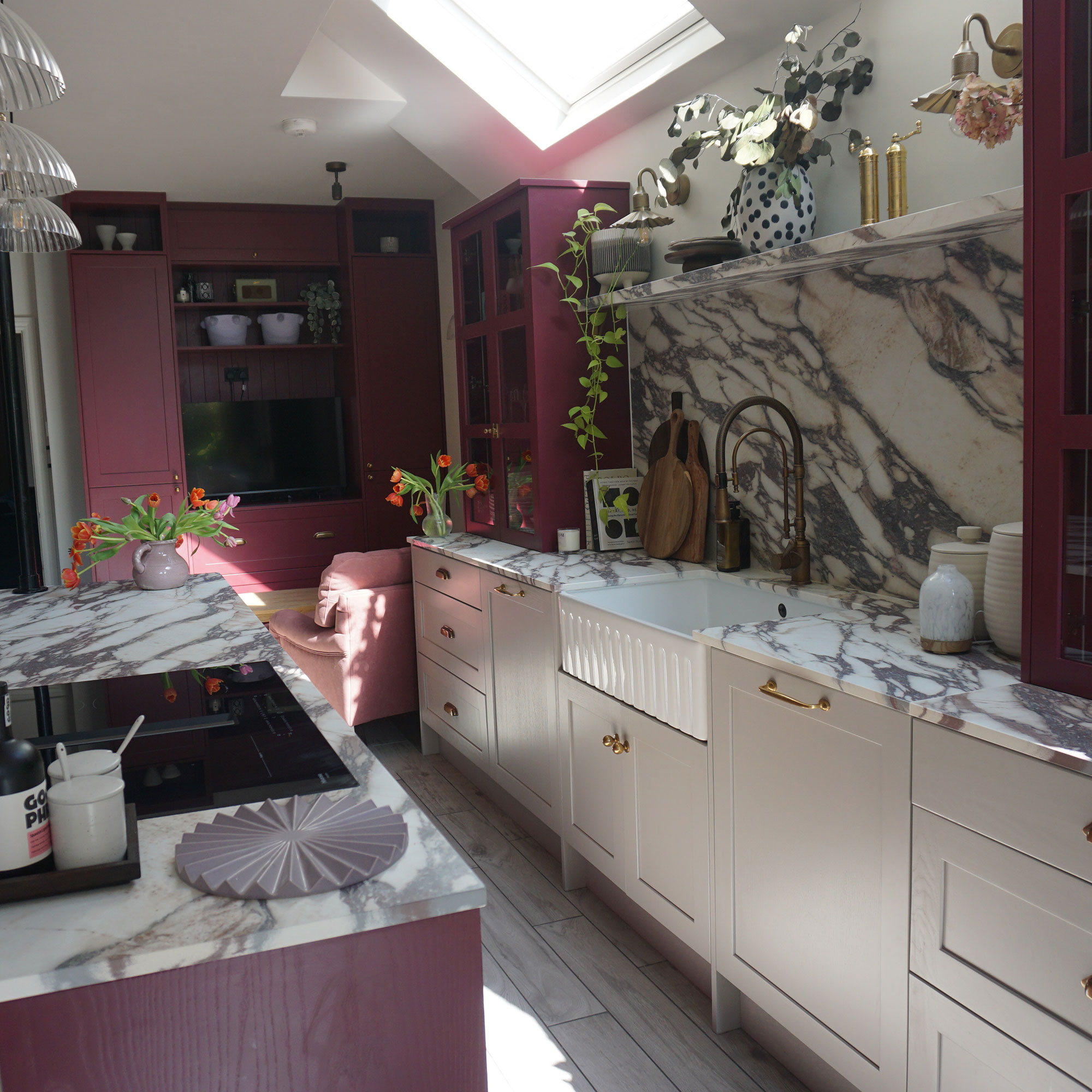 Marble kitchen worktop run with deep fluted Belfast sink, marble splashback and red cabinetry across from marble topped island with integrated hob