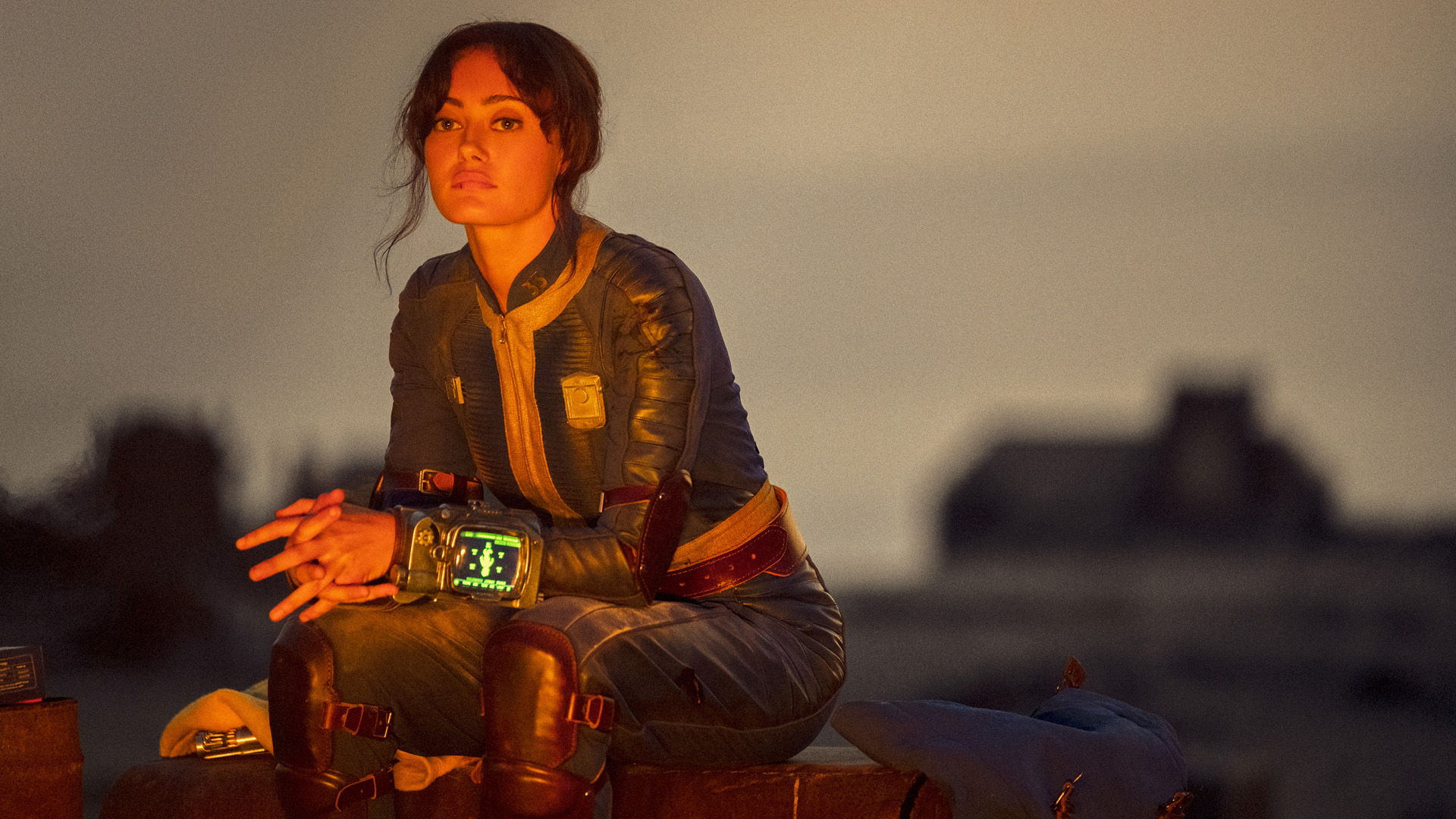 Lucy sits by a campfire as dusk sets in during Amazon's Fallout TV show